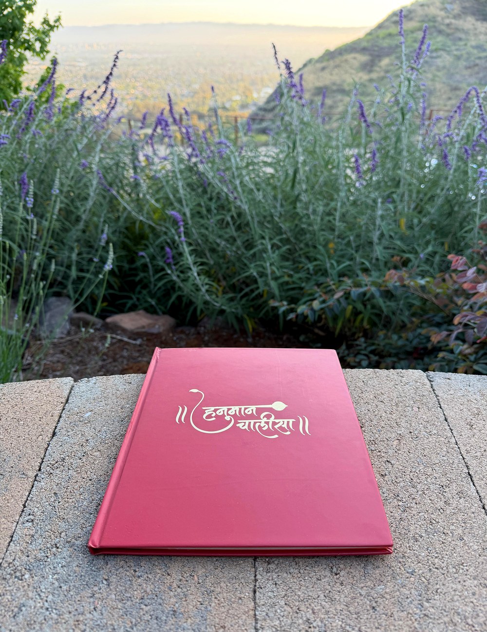 Hanuman Chalisa collector's edition — hardcover book on stone wall, lavender and hills at dusk